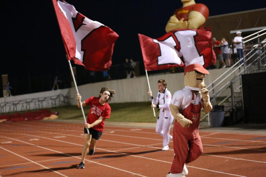 The Miller Man leads senior Jackson Wolf and sophomore Harrison Hines around a curve as several of the flag runners head back towards the student section.