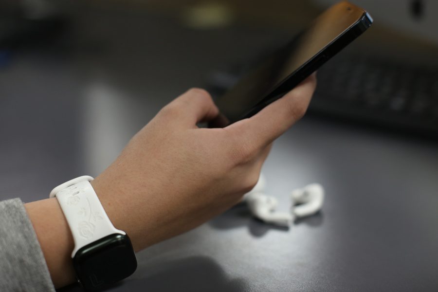 Yukon student swipes on iPhone while wearing an Apple watch with AirPods pros sitting behind her.