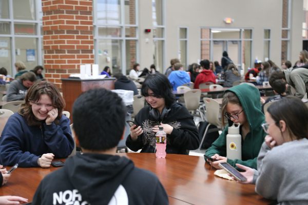 Sitting in the cafeteria with friends during sixth hour lunch, freshmen Olivia Ward, Klaire Miller and Haylee Romines, spent time on their phones with occasional side conversations. Social media played a role in social settings as it contributed to online conversations and built a barrier when having a face-to-face conversation. (Photo by Carmen Osio Rodriguez)